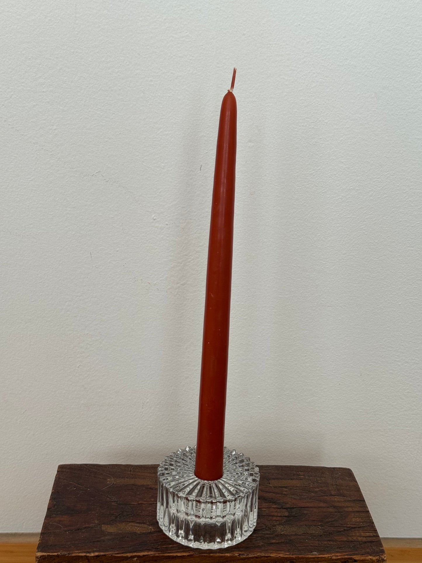 Brown candle in a clear glass holder on a wooden base against a white wall