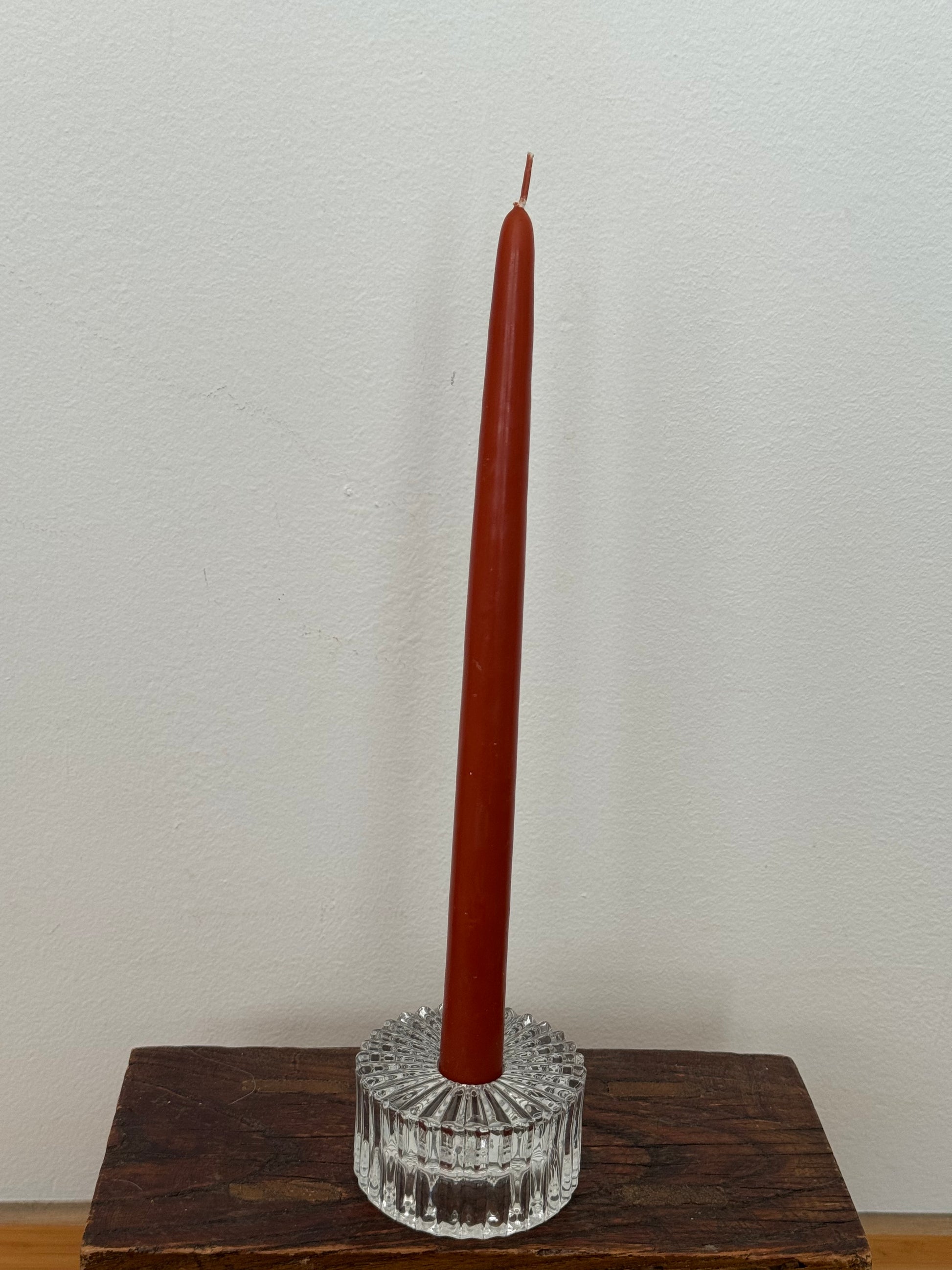 Brown candle in a clear glass holder on a wooden base against a white wall