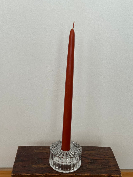 Brown candle in a clear glass holder on a wooden base against a white wall