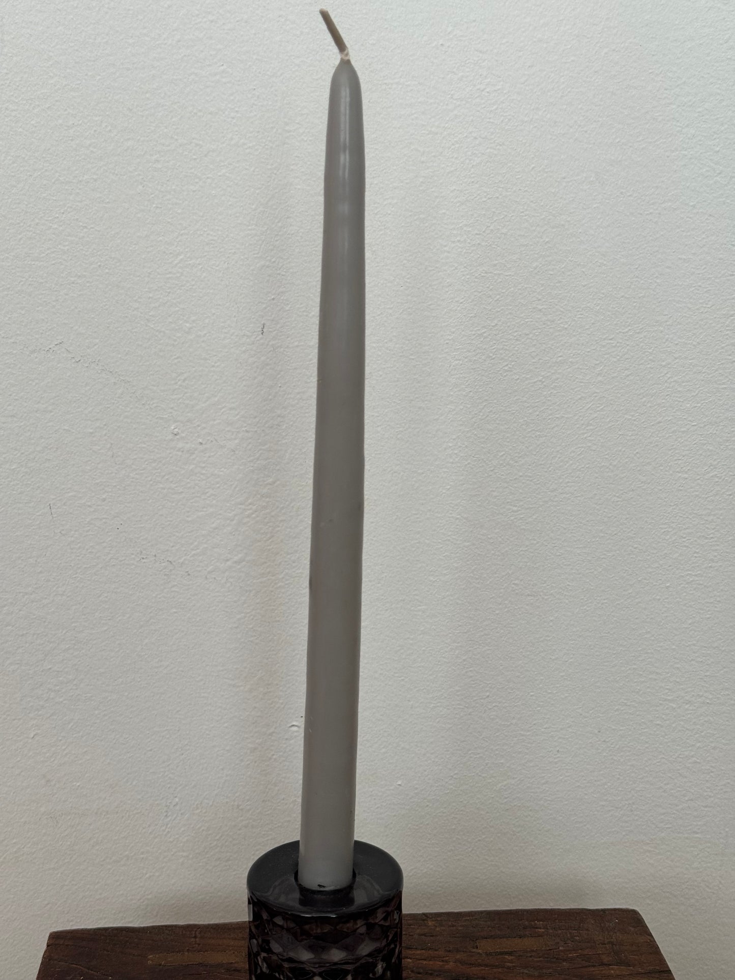 Gray candle on a wooden stand against a white wall