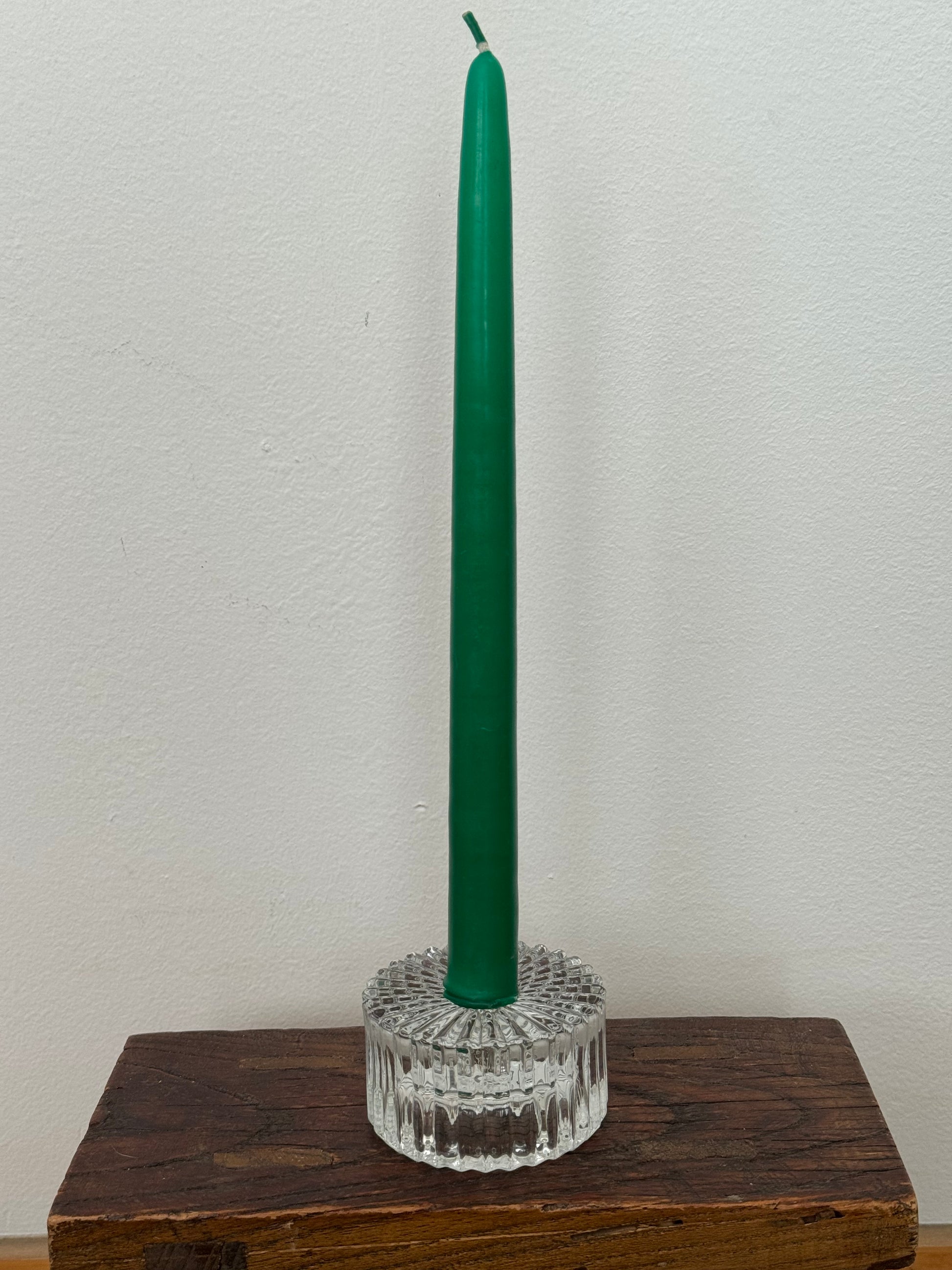 Green candle in a decorative holder on a wooden surface with a white background