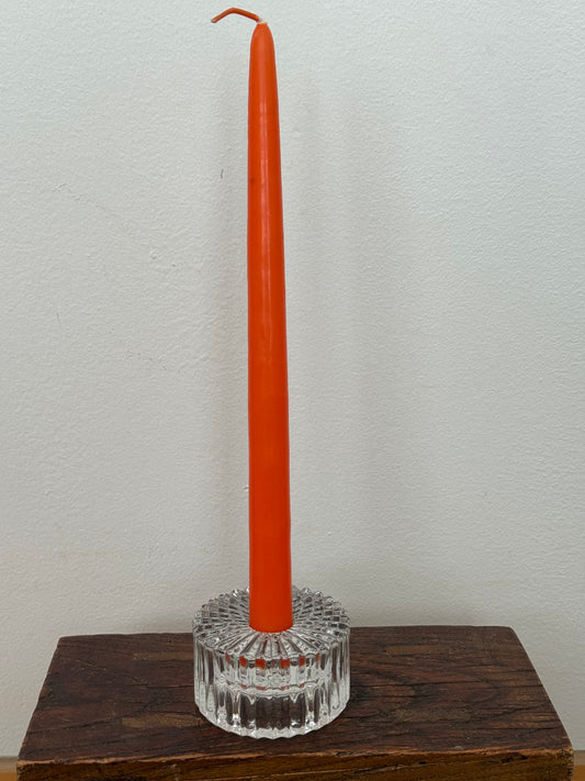 Orange candle in a clear glass holder on a wooden surface with a white background