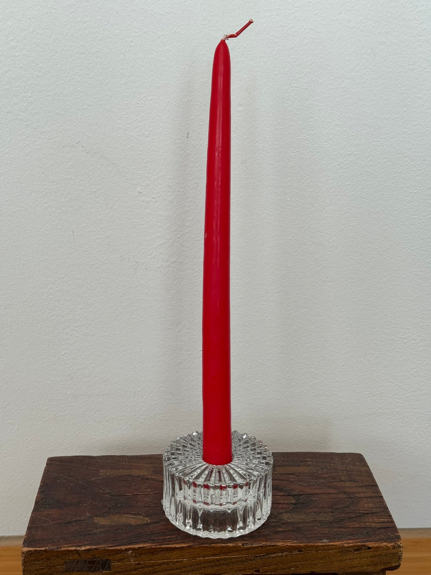 Red candle in a crystal holder on a wooden surface with a white background