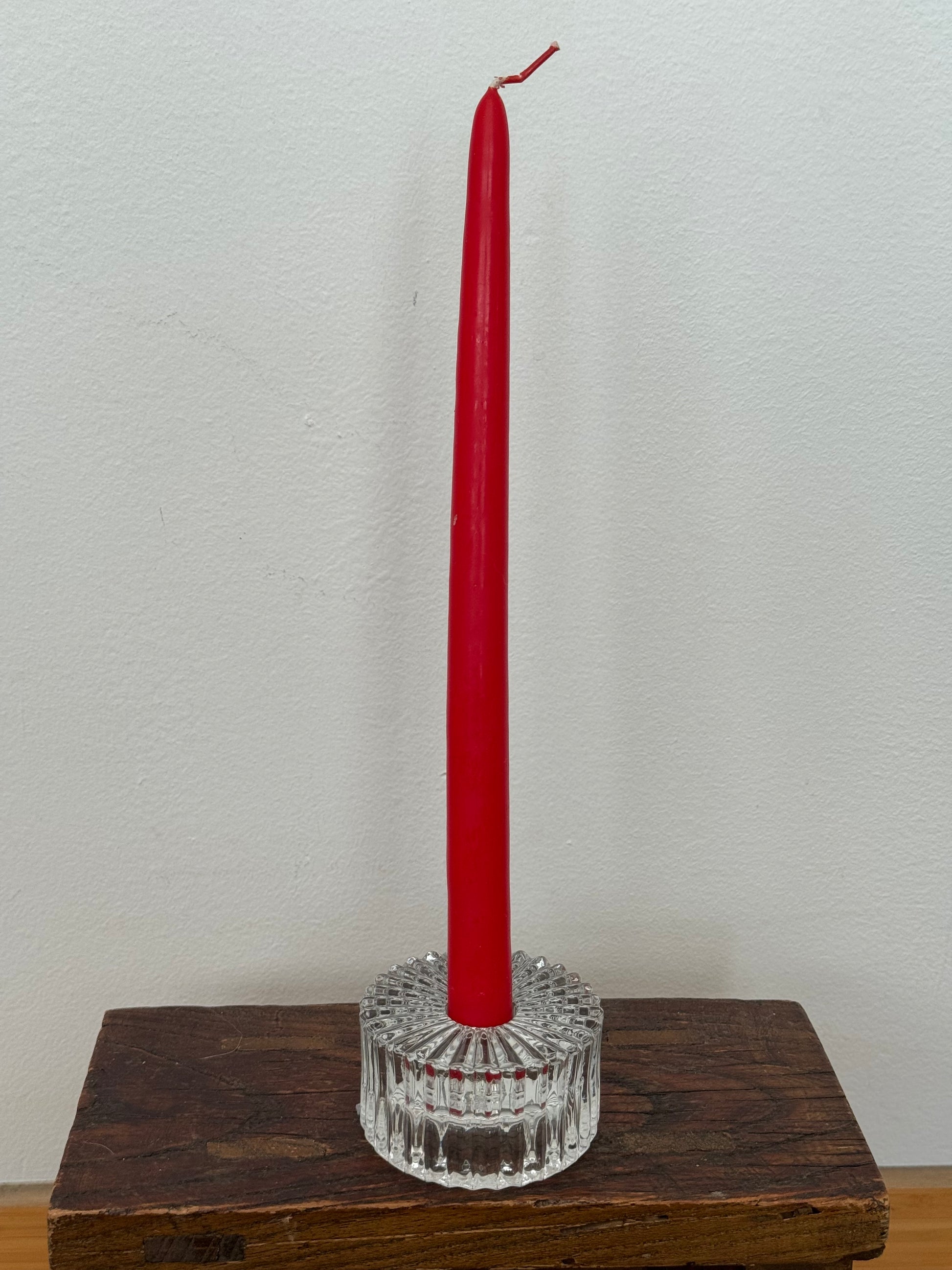 Red candle in a crystal holder on a wooden surface with a white background